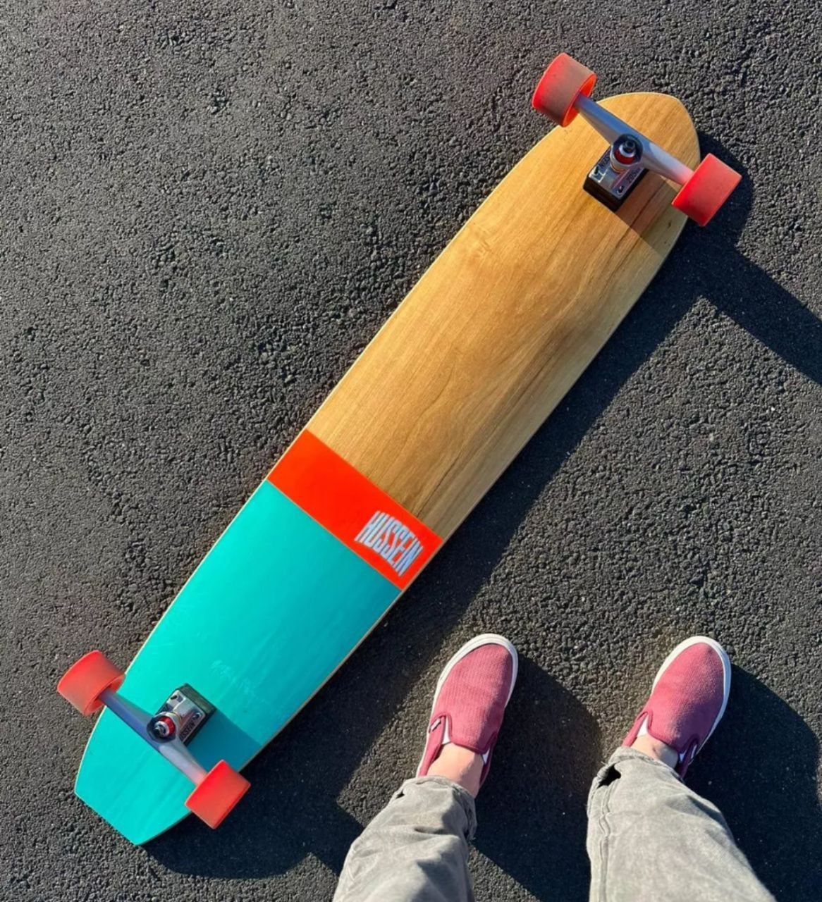 Board teal e laranja Hussein no asfalto — rodas vermelhas